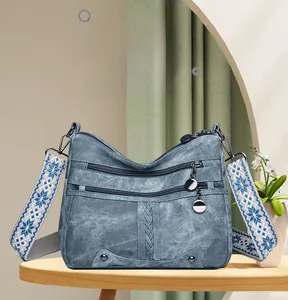 Detailed view of blue denim texture crossbody bag with metal ring zippers and patterned strap