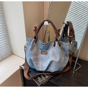 Detail of light blue denim tote bag with brown leather handles and wide shoulder strap