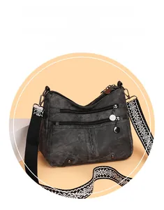 Detail of dark gray soft leather crossbody bag featuring a patterned wide strap and pockets