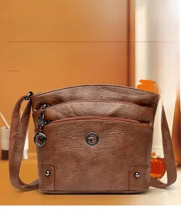 Détail macro du sac bandoulière en cuir marron avec trois fermetures éclair et logo kangourou