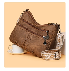 Detail view of brown multi-zipper crossbody bag with floral embroidered strap and metal charms