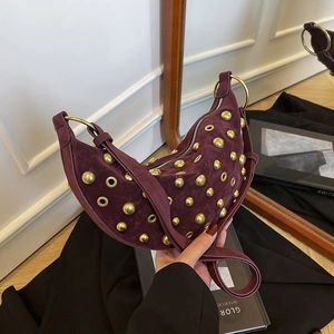 Sac demi-lune en daim bordeaux avec rivets dorés présenté dans un décor artistique