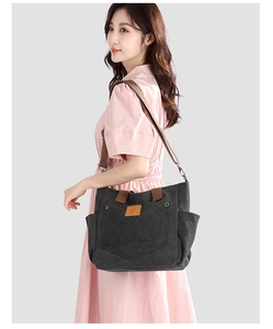 Side view of dark canvas tote bag with brown leather handles and adjustable shoulder strap