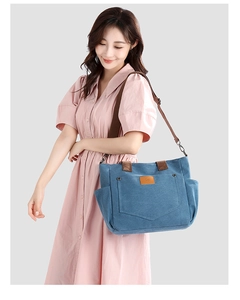 Blue canvas tote bag with brown leather handles and adjustable strap worn by a model