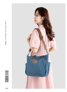 Blue canvas tote bag with brown straps and leather logo patch shown on a model