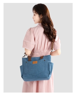 Detail view of blue canvas tote bag featuring side pockets and a brown leather logo patch
