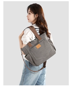 Close-up of a large grey canvas tote bag with brown straps and leather logo patch