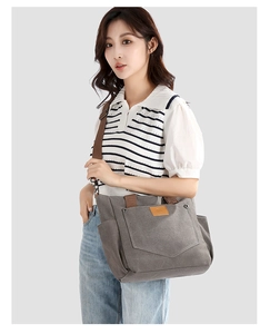 Detail of grey canvas tote bag with adjustable brown shoulder strap and leather logo patch