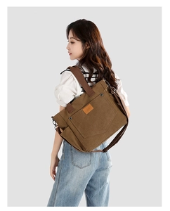 Detail of a brown canvas tote bag with side pockets and a leather logo on a model