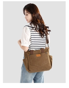 Detailed side view of brown canvas shoulder bag with large front pocket and logo patch