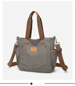 Detail of grey canvas tote bag featuring brown woven handles and adjustable shoulder strap