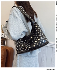 Détail d'un sac à bandoulière en cuir noir avec rivets argentés porté par un mannequin