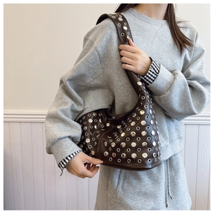 Détail d'un sac demi-lune marron foncé avec rivets argentés porté à l'épaule
