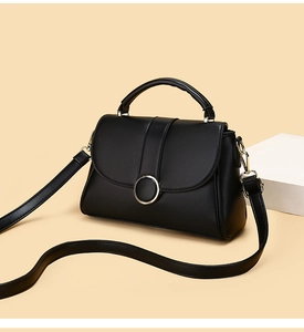 Close-up of black leather handbag featuring a glossy circular metal buckle and fine texture