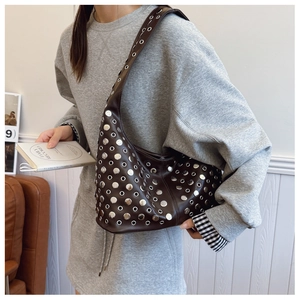 Détail du sac hobo marron foncé avec œillets et rivets argentés porté à l'épaule