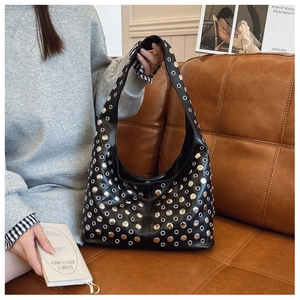 Détail d'un sac seau punk noir avec des rivets et œillets métalliques argentés sur un canapé