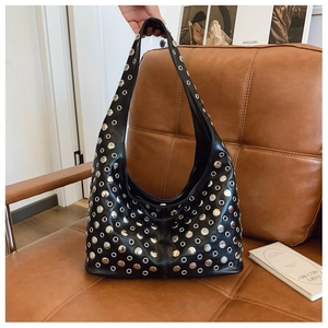 Détail du sac hobo en cuir noir avec rivets métalliques argentés sur fond en cuir brun