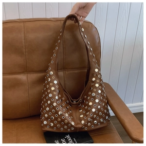 Gros plan du sac hobo en cuir marron orné de clous métalliques argentés et d'oeillets