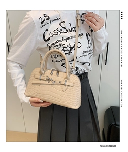 Detail shot of cream crocodile embossed handbag with metal buckles and long shoulder strap