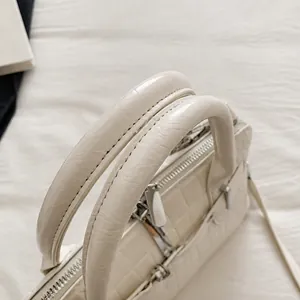 Detailed close-up of cream white crocodile embossed leather handbag with round top handles