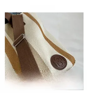 Detail of striped canvas tote bag featuring brown leather logo and adjustable strap