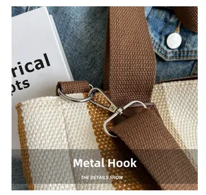 Detail of silver metal swivel hook and textured striped canvas on a crossbody tote bag