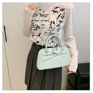 Detail view of mint green crocodile pattern handbag with silver zippers and long strap