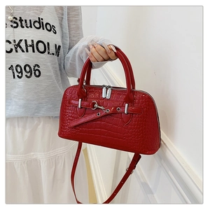 Close-up of red crocodile-embossed handbag with dual silver zippers and a long strap
