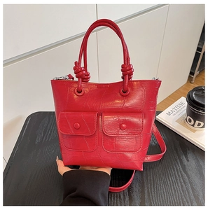 Detail of red crocodile texture handbag with two front pockets and knotted handle decor
