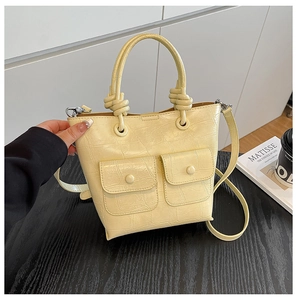 Detail view of cream crocodile-embossed handbag featuring dual front pockets and knotted handles