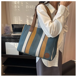 Detail of striped canvas tote bag featuring green and yellow stripes with leather logo