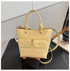 Detail of a creamy yellow crocodile-embossed handbag with knot handle on a desk