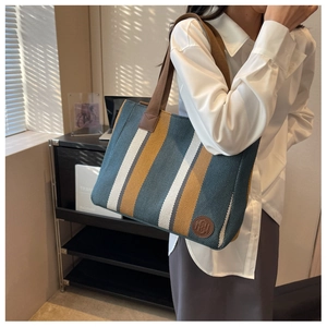 Close-up of vertical striped canvas tote bag with brown logo patch and woven handles