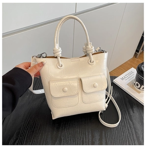 Detail of cream bucket bag featuring crocodile pattern, twist handle and small twin pockets