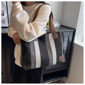 Detail of striped canvas tote bag showing the leather logo patch and brown woven handle