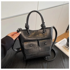 Detail of black crocodile texture bucket bag with knotted handle and double front pockets