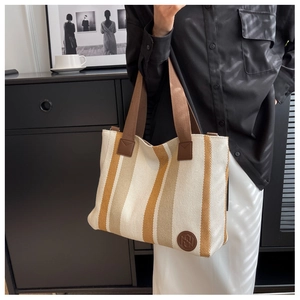 Close-up of a yellow striped canvas tote bag with brown handles and a round leather logo