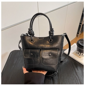 Detail of black crocodile texture handbag with decorative front pockets and knot handles
