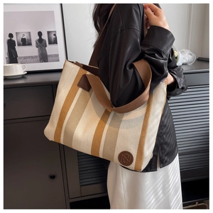 Close-up of canvas tote bag featuring brown stripes and leather logo on a wooden background