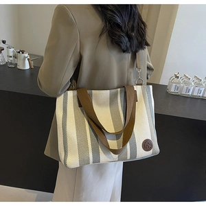 Detail of striped canvas tote bag with wide shoulder strap shown on a model