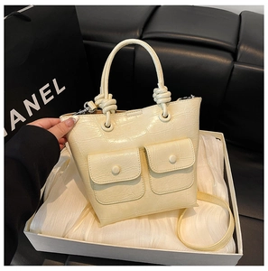 Detailed close-up of cream handbag with crocodile texture and unique knotted handle design