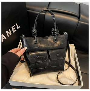 Detail of black crocodile embossed handbag with knot handle and front flap pockets