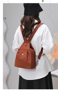 Zaino in nylon marrone caramello su modella con sfondo grigio minimalista