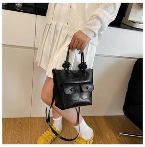 Detail of black crocodile pattern tote bag featuring knotted handles and dual front pockets