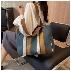 Detail of multi-color striped canvas tote bag with brown shoulder strap and leather logo