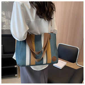 Detailed side view of striped canvas tote bag featuring leather logo patch and sturdy handles