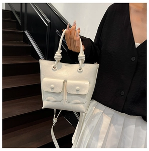 Close-up of white crocodile pattern handbag featuring knot handles and front flap pockets