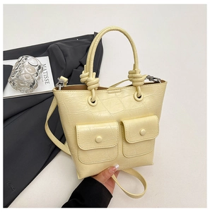 Detail of light yellow crocodile texture handbag with buckle pockets and knot handle