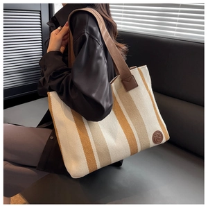 Detailed view of striped canvas tote bag with brown straps and leather logo patch