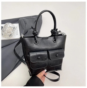 Detail of black crocodile texture handbag with front flap pockets and knotted handle